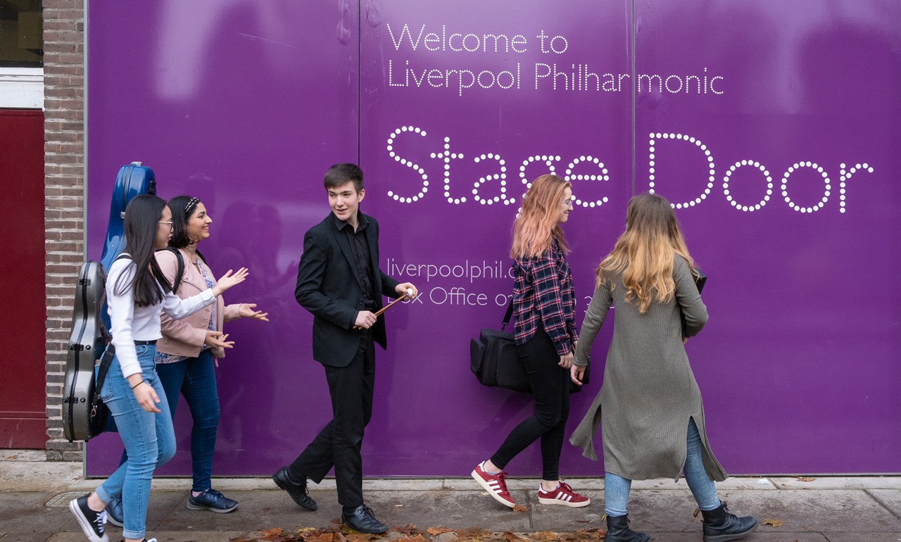 smiling youth company members in fronr of a purple stage door
